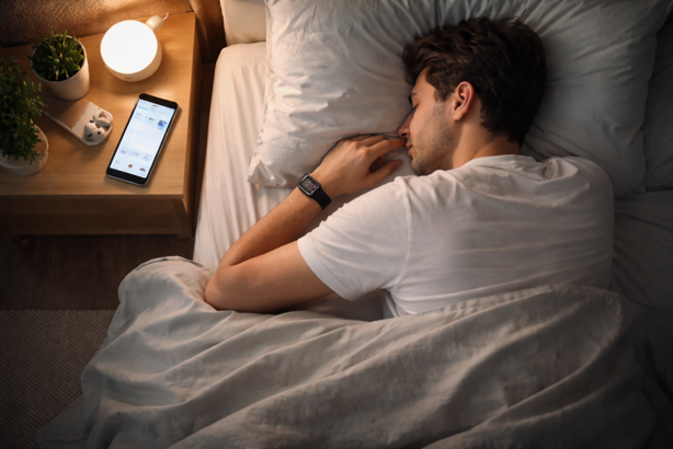 person sleeping with fitness tracker on wrist, displaying sleep tracking data on bedside smartphone