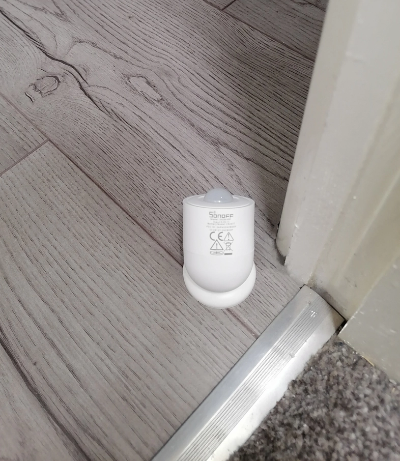 sonoff snzb-03p motion sensor on floor beside door frame and carpet threshold