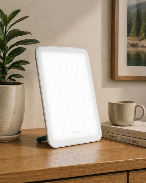 lumie vitamin l light therapy lamp on a wooden surface with a plant and coffee cup