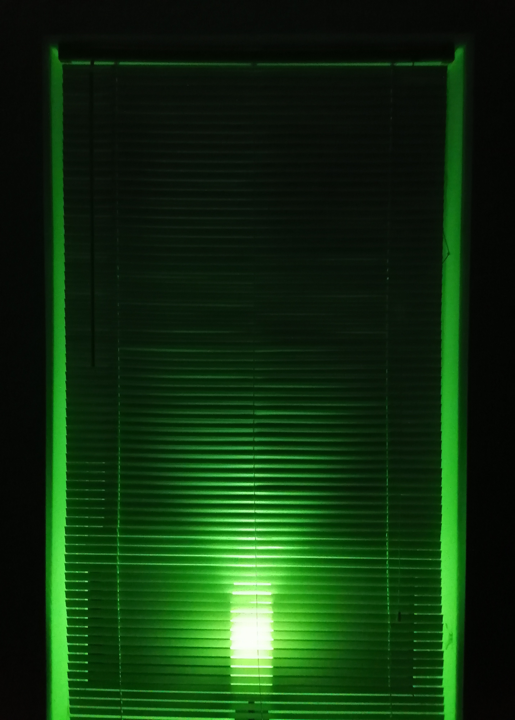 green light glowing through closed window blinds at night