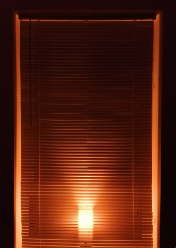 orange light glowing through closed window blinds at night
