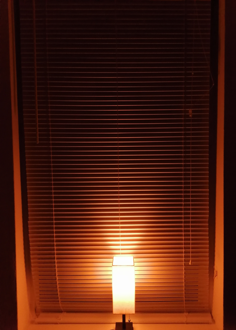 table lamp glowing orange in front of closed window blinds